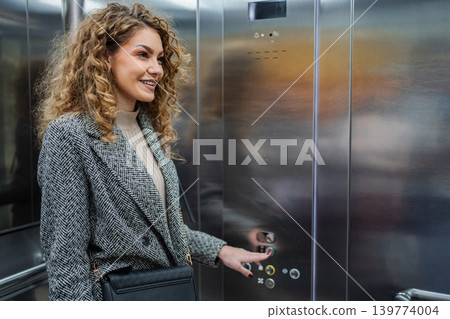 Smiling woman pressing elevator button in office building Smiling woman pressing elevator button in office building 139774004