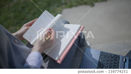 A close-up shot of a hand-held girl holding a pen and leafing through a notebook with handwritten notes. 139774251