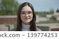 Close-up portrait of a young white female student wearing glasses with long dark hair in a park 139774253
