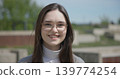 Close-up portrait of a young white female student wearing glasses with long dark hair in a park 139774254
