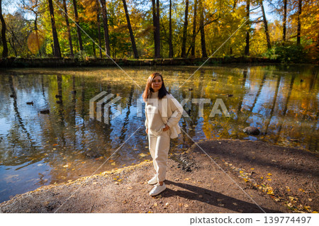 Woman hiking on nature trail near pond in autumn forest. Girl enjoying fall season walk in woods. Active lifestyle, leisure activity, tranquil journey in colorful parkland landscape. Woman hiking on nature trail near pond in autumn forest. Girl enjoying fall season walk in woods. Active lifestyle, leisure activity, tranquil journey in colorful parkland landscape. 139774497