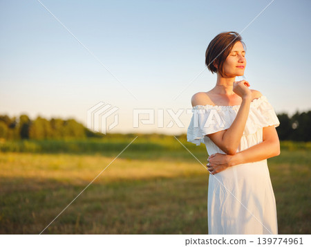 Woman in white dress walking through sunset field in Croatia Woman in white dress walking through sunset field in Croatia 139774961