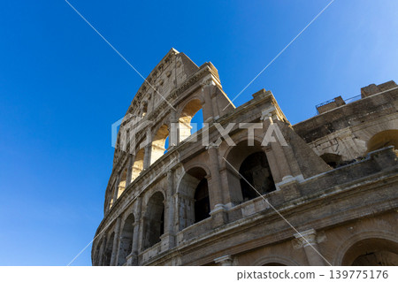 Famous Coliseum in Rome. Colosseum, or Coliseum. Part of the wall of an antique stone structure with arches. Italy, Europe. Famous touristic place in the world, Europe. Beautiful blue sky background. Famous Coliseum in Rome. Colosseum, or Coliseum. Part of the wall of an antique stone structure with arches. Italy, Europe. Famous touristic place in the world, Europe. Beautiful blue sky background. 139775176