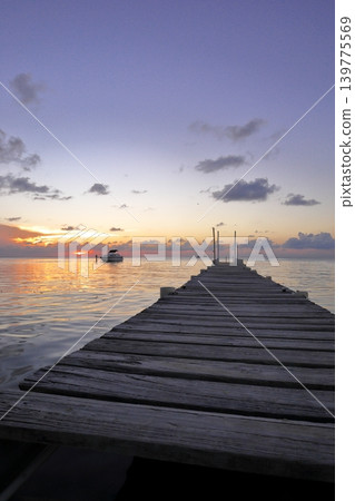 A sunset over Caye Caulker Island: a calm sea with boats floating on it and a wooden pier. A sunset over Caye Caulker Island: a calm sea with boats floating on it and a wooden pier. 139775569