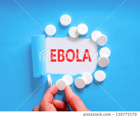Ebola virus medical words symbol. Concept word Ebola on beautiful white paper. Beautiful blue background. Beautiful white pills. Doctor hand. Medical Ebola virus concept. Copy space. Ebola virus medical words symbol. Concept word Ebola on beautiful white paper. Beautiful blue background. Beautiful white pills. Doctor hand. Medical Ebola virus concept. Copy space. 139775579