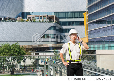 Construction supervisor talking on smartphone while coordinating workers and managing operations at modern construction site. Construction supervisor talking on smartphone while coordinating workers and managing operations at modern construction site. 139775793