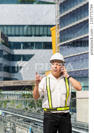 Construction supervisor talking on smartphone while coordinating workers and managing operations at modern construction site. Construction supervisor talking on smartphone while coordinating workers and managing operations at modern construction site. 139775794