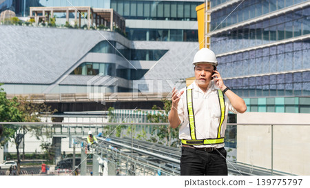 Construction supervisor talking on smartphone while coordinating workers and managing operations at modern construction site. Construction supervisor talking on smartphone while coordinating workers and managing operations at modern construction site. 139775797
