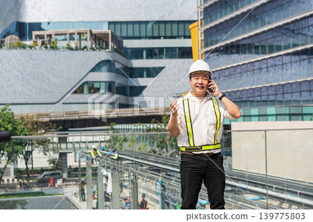 Construction supervisor talking on smartphone while coordinating workers and managing operations at modern construction site. Construction supervisor talking on smartphone while coordinating workers and managing operations at modern construction site. 139775803