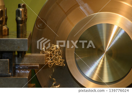 Close-up of a long continuous spiral metal chip attached and tangled on a lathe cutting tool during the turning process. 139776024