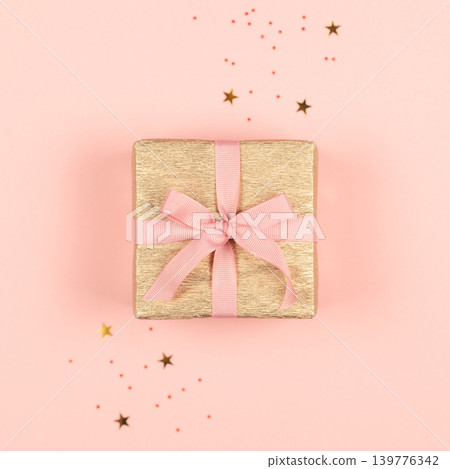 Golden gift box with pink bow on the pink background with sparkles. Golden gift box with pink bow on the pink background with sparkles. 139776342