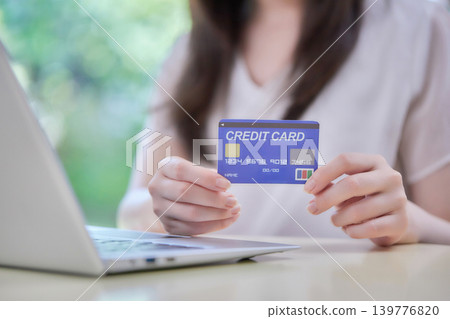 A woman in her 20s enters information into a computer while looking at her credit card. A woman in her 20s enters information into a computer while looking at her credit card. 139776820
