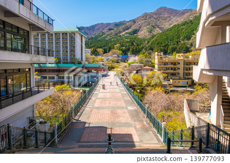Nikko City, Tochigi Prefecture: A view of Kinugawa Onsen and Fureai Bridge stretching towards the mountains with their fresh green leaves and a clear blue sky. 139777093