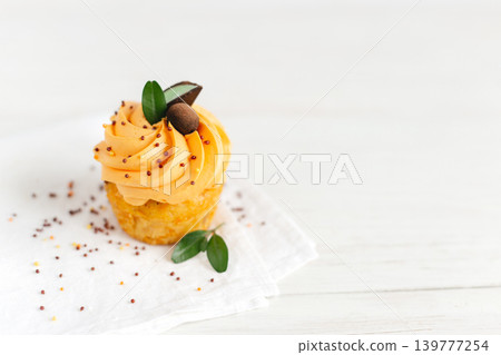 Tasty pumpkin cupcake with orange cream and decoration on white wooden table. Place for text. Tasty pumpkin cupcake with orange cream and decoration on white wooden table. Place for text. 139777254