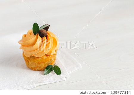 Tasty pumpkin cupcake with orange cream and decoration on white wooden table. Tasty pumpkin cupcake with orange cream and decoration on white wooden table. 139777314