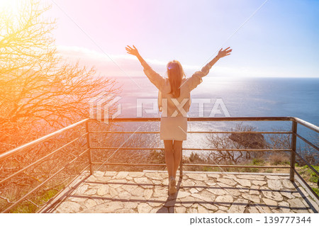 Woman ocean freedom young woman stands on a scenic overlook with arms raised towards the sea at sunrise with copy space Woman ocean freedom young woman stands on a scenic overlook with arms raised towards the sea at sunrise with copy space 139777344