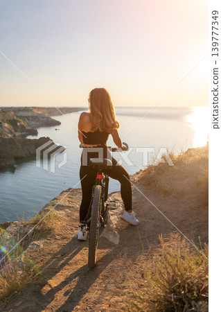 Cycling Cliff Sunset Young woman sitting on her mountain bike at the edge of a coastal cliff overlooking the ocean during sunset 139777349