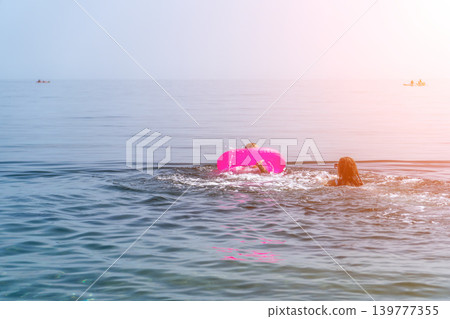 Swimming vacation ocean woman and child playing with a pink inflatable ring in the blue sea water during a sunny summer day Swimming vacation ocean woman and child playing with a pink inflatable ring in the blue sea water during a sunny summer day 139777355