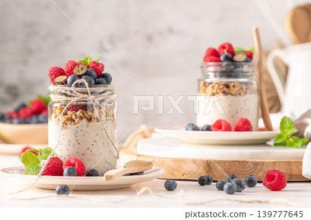 Nutritious overnight oats and chia seed pudding layered with granola and topped with fresh raspberries and blueberries in rustic glass jars on a bright table with wooden accents Nutritious overnight oats and chia seed pudding layered with granola and topped with fresh raspberries and blueberries in rustic glass jars on a bright table with wooden accents 139777645