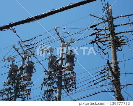 A simple background of utility poles and power lines stretching against a blue sky. 139777722