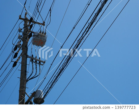 A simple background of utility poles and power lines stretching against a blue sky. 139777723