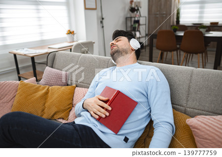 Man with wireless headphones fell asleep while reading a book at home Man with wireless headphones fell asleep while reading a book at home 139777759