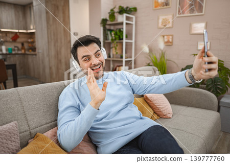 Man with wireless headphones talking on a video call at home Man with wireless headphones talking on a video call at home 139777760