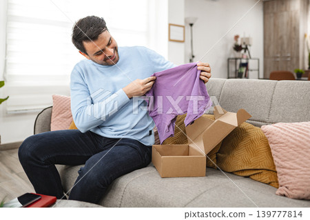 Man opens the cardboard package and looks at the new T-shirt 139777814
