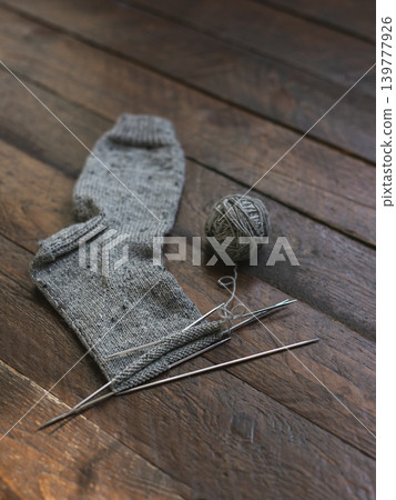 Hand knitted sock with needles and grey yarn ball on dark wooden background. Hand knitted sock with needles and grey yarn ball on dark wooden background. 139777926
