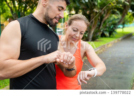 Fit couple checking smart watch during outdoor workout in tropical park Fit couple checking smart watch during outdoor workout in tropical park 139778022