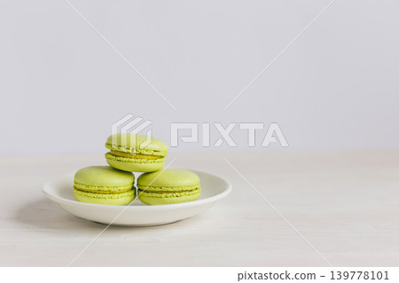 Three light green french macarons on a white plate and wooden table. Pistachio macarons. Three light green french macarons on a white plate and wooden table. Pistachio macarons. 139778101