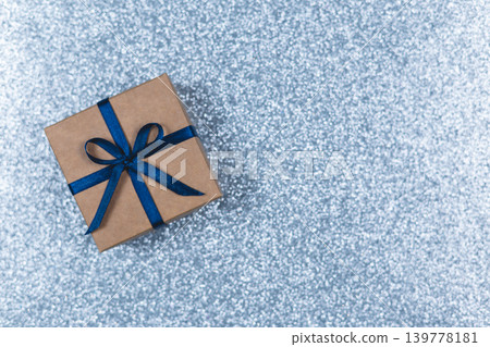 Craft gift box with blue bow on sparkle light blue background. Holiday concept. Craft gift box with blue bow on sparkle light blue background. Holiday concept. 139778181