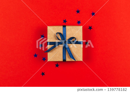 Craft gift box with blue bow on red background with blue stars. Holiday concept. Craft gift box with blue bow on red background with blue stars. Holiday concept. 139778182
