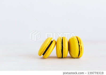 Three yellow french macarons on a wooden table. Banana macarons with chocolate cream. White background. Three yellow french macarons on a wooden table. Banana macarons with chocolate cream. White background. 139778319