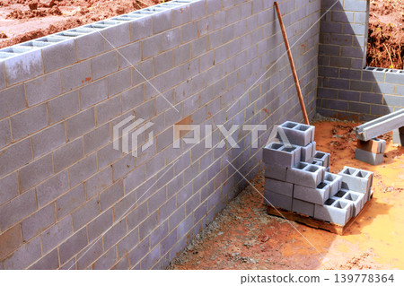 Workers are building cement block wall at construction site with stacks of blocks on ground Workers are building cement block wall at construction site with stacks of blocks on ground 139778364