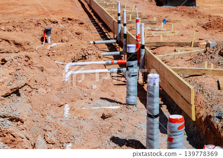 Workers prepare site for new building, installing plumbing fixtures in ground before foundation work begins. 139778369