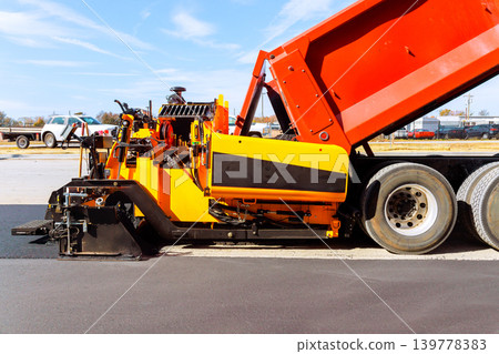 Asphalt paving machine works to lay down asphalt on road in construction site at city. Asphalt paving machine works to lay down asphalt on road in construction site at city. 139778383