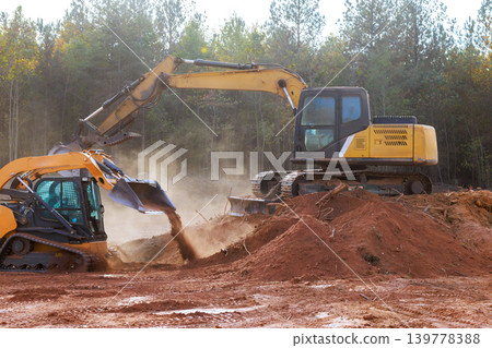 Workers operate construction machinery to move dirt at site surrounded by dust Workers operate construction machinery to move dirt at site surrounded by dust 139778388