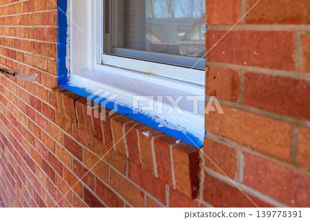 Workers apply blue tape around window on brick wall during painting window frame Workers apply blue tape around window on brick wall during painting window frame 139778391