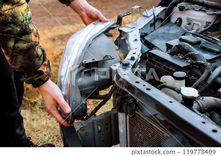 Worker focuses on taking off old headlight from car's front while standing outside Worker focuses on taking off old headlight from car's front while standing outside 139778409