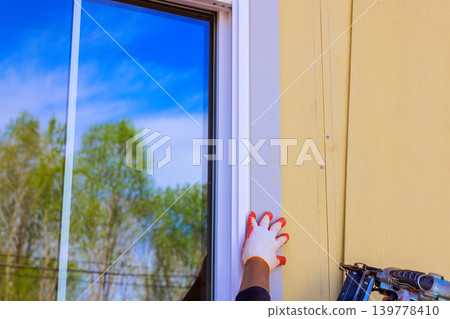 Builder uses nail gun to adjust window trim frame setting is outdoors Builder uses nail gun to adjust window trim frame setting is outdoors 139778410