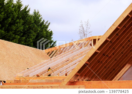 Workers construct roof frame using wooden beams trusses in residential area 139778425