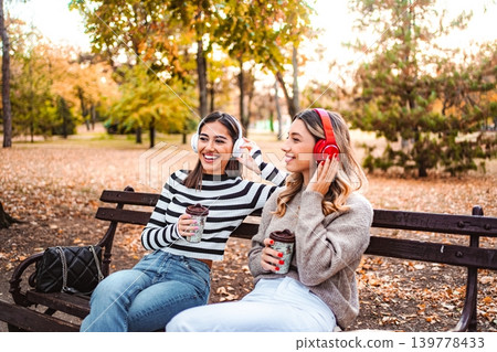 Two girls enjoying autumn vibes while sipping coffee in the park Two girls enjoying autumn vibes while sipping coffee in the park 139778433