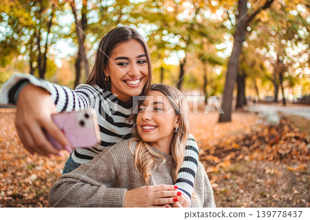 Joyful girls capturing autumn memories together in a colorful park Joyful girls capturing autumn memories together in a colorful park 139778437
