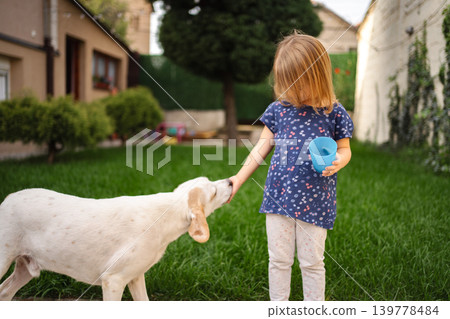 Joyful moments between a child and her playful dog in a sunny yard Joyful moments between a child and her playful dog in a sunny yard 139778484