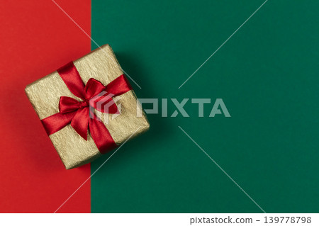 Golden gift box with red bow on the red and green background. Holiday concept. Golden gift box with red bow on the red and green background. Holiday concept. 139778798
