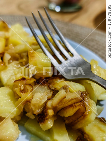 Fried potato and onion pieces are served on a blue plate. A fork rests on the food, showing a simple meal ready to eat Fried potato and onion pieces are served on a blue plate. A fork rests on the food, showing a simple meal ready to eat 139778895