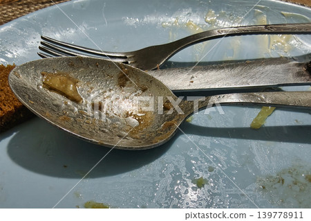 A table shows used utensils and food remnants after a meal. Forks and spoons lay on a blue plate, signaling the end of dining and chatting A table shows used utensils and food remnants after a meal. Forks and spoons lay on a blue plate, signaling the end of dining and chatting 139778911