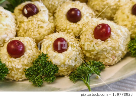 A plate holds small round food items covered in sesame seeds, topped with red grapes, and garnished with parsley during a casual evening gathering at a home A plate holds small round food items covered in sesame seeds, topped with red grapes, and garnished with parsley during a casual evening gathering at a home 139778923