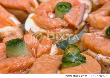 Several pieces of toasted bread topped with cream cheese, smoked salmon, and rolled green onion sit ready to be served at a social event in the evening Several pieces of toasted bread topped with cream cheese, smoked salmon, and rolled green onion sit ready to be served at a social event in the evening 139778925